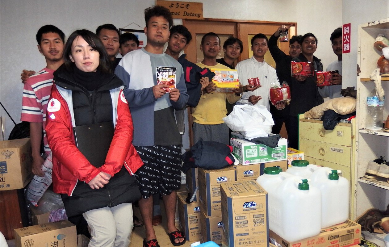 AAR staff and Indonesian men stand side by side holding relief supplies delivered by AAR.